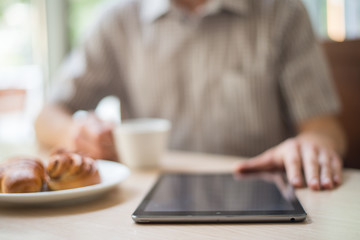 Man with tablet computer reading news at motning in cafe