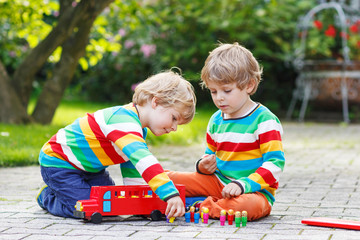Two siblings, kid boys playing with red school bus