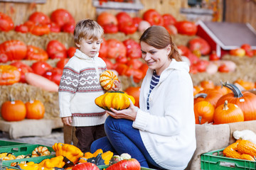 Young mother and her little son playing on pumpkin patch farm.