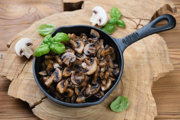Frying pan with roasted champignons, rustic wooden background