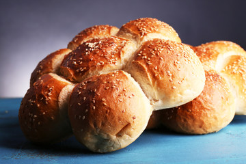 Tasty buns with sesame on color wooden table, on gray