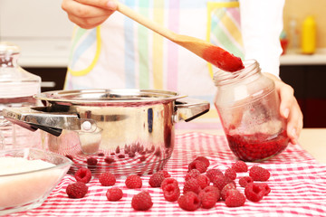 Woman cooking raspberry jam in kitchen