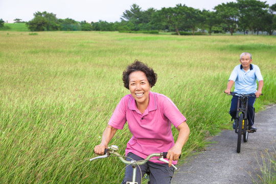 Happy asian seniors couple biking in the park.