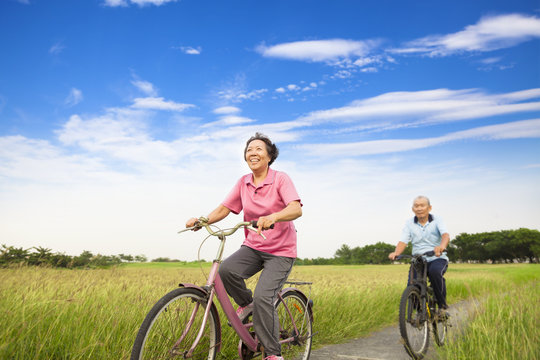 Happy Asian elderly seniors couple biking in farm