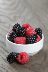 ripe blackberries and raspberries in white bowl on old oak table