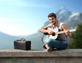Young guitarist sitting on parapet and smiling at camera