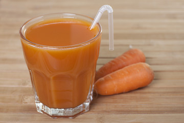 Carrot juice in a glass and carrots on the table.