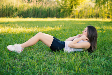 Naklejka na ściany i meble Young woman portrait practicing abdominal exercise outdoors in a
