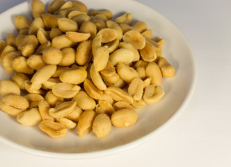 Salty peanuts on a white plate on a white background