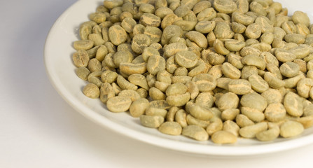 Green coffee grains on a white plate on a white background