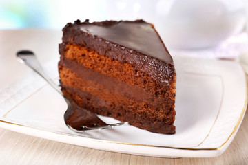 Piece of chocolate cake on saucer on light background