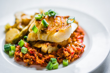 Roasted hake with romesco sauce and onion on wooden background