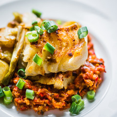 Roasted hake with romesco sauce and onion on wooden background