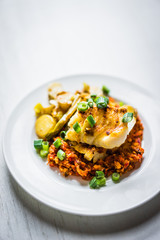 Roasted hake with romesco sauce and onion on wooden background