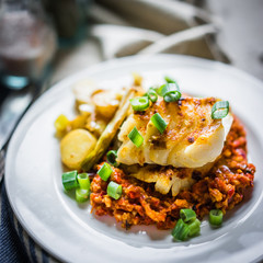 Roasted hake with romesco sauce and onion on wooden background