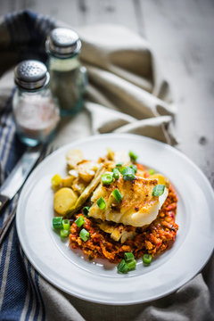 Roasted hake with romesco sauce and onion on wooden background