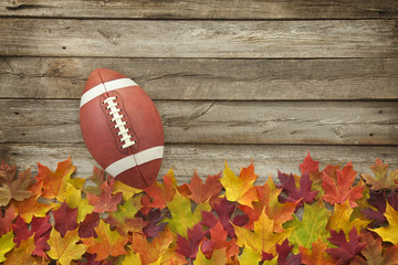 Football with fall leaves on rough wood top view