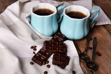 Cups of coffee with chocolate and napkin on wooden table