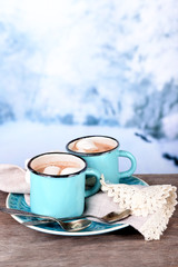 Cups of tasty hot cocoa, on wooden table, on light background