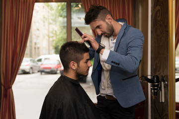 Male Hairdresser Cutting Hair Of Smiling Man Client