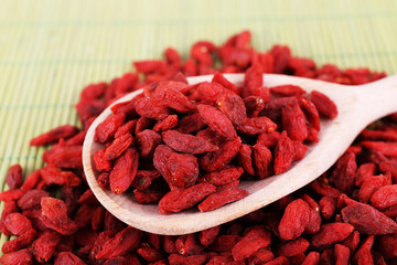 Goji berries in wooden spoon on bamboo mat background