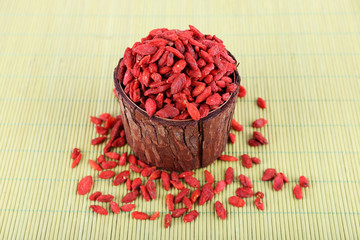 Goji berries in wooden bowl on bamboo mat background