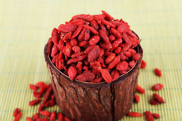 Goji berries in wooden bowl on bamboo mat background