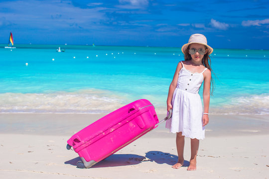 Little adorable girl with big luggage in hands on tropical beach