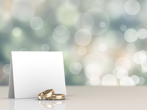 A pair of gold wedding rings and a card with bokeh background