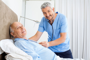 Fototapeta premium Portrait Of Smiling Caretaker Examining Senior Man