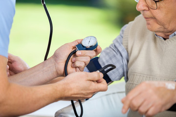 Male Caretaker Measuring Blood Pressure Of Elderly Man