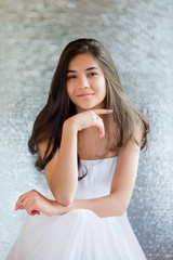 Beautiful biracial teen girl in white dress sitting, thinking
