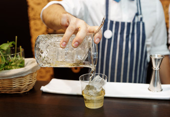 Bartender is making cocktail at bar counter, toned