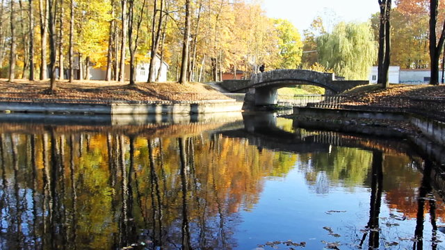 lonely man walks along small stone bridge over lake in park