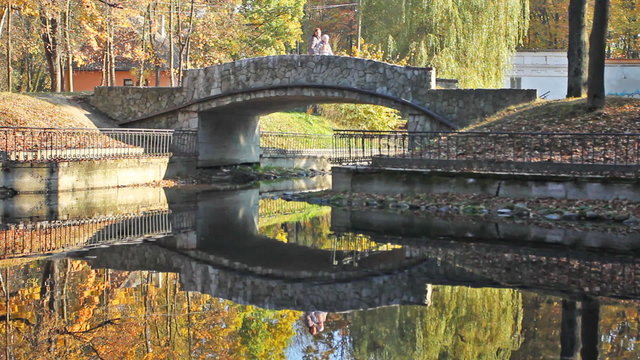 mother and teen girl on small stone bridge over lake in park
