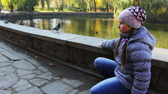 cute teen girl sits and luring pigeon pop-corn on hand near lake