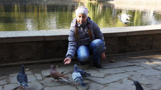 cute teen girl siting feeds pop-corn pigeons in autumn near lake