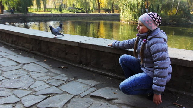 teen girl sits and luring pigeons throwing pop-corn near lake