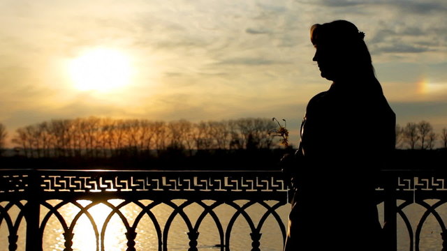 silhouette of lady with flower near clear lake, sunset, close-up