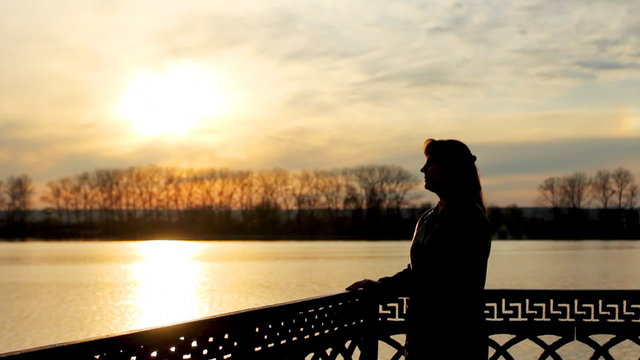 silhouette of pretty lady with flower near clear lake, sunset