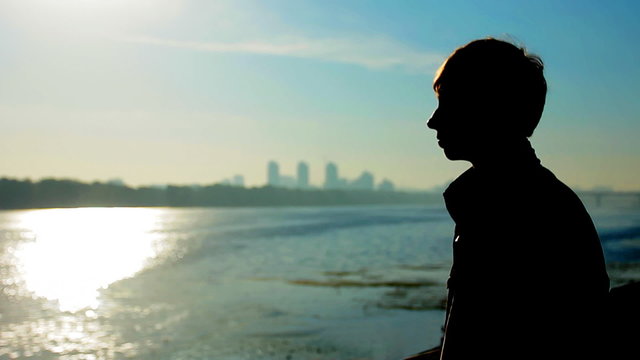 young guy near wide river, silhouette against sunrise, closeup