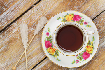 Tea in vintage cup and sugar sticks on wooden surface
