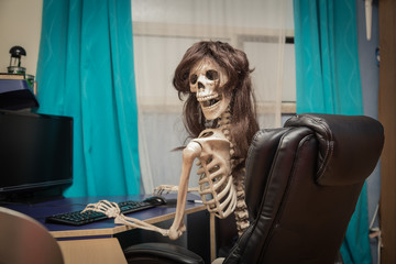 smiling skeleton on black leather chair behind the desktop