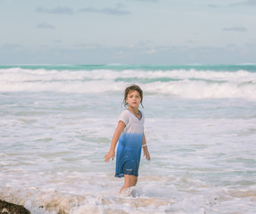 Fototapeta na wymiar Child girl walking in the ocean near the beach on sunny day