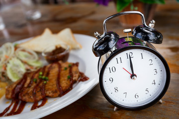 Clock on Wooden Table with steak on background, Lunch Time Conce