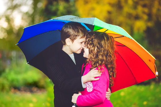 Little girl and boy hiding under an rainbow umbrella from the ra