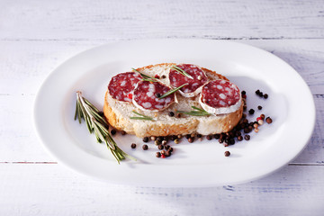 Sandwich with salami on plate on wooden background