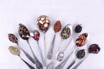 Tea in metal spoons on fabric background