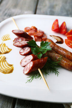 Assortment of tasty thin sausages on plate, on wooden