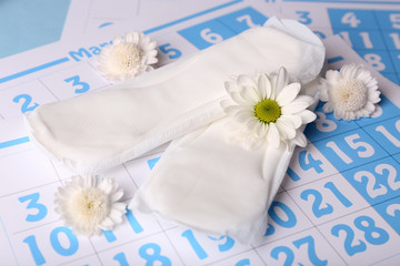 Sanitary pads and white flowers on blue calendar background